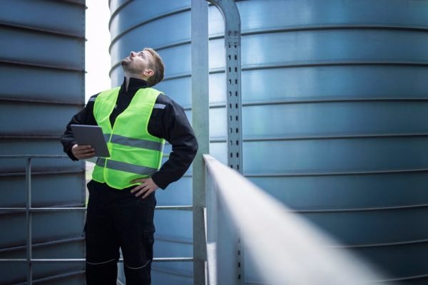 factory-worker-standing-metal-platform-industrial-storage-tanks-looking-up-visual-inspection-silos-food-production_342744-450